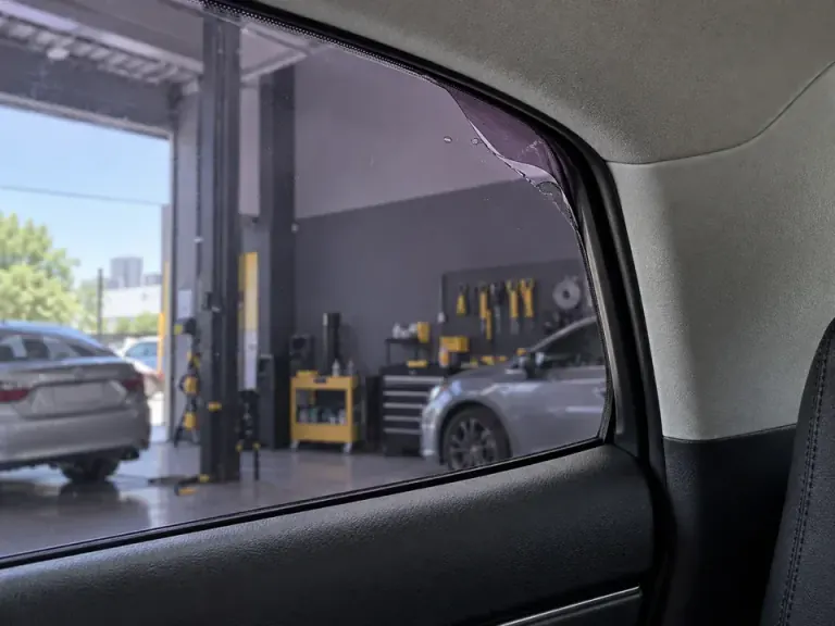 Película antiga descolando na borda do vidro de um carro, antes da remoção